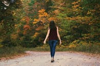 Woman in Brown Sleeveless Dress and Blue Jeans Standing on Gray Path Road